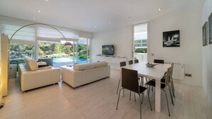 Een moderne woonkamer met een eethoek, grote ramen en een flatscreen televisie.
