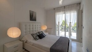 Een slaapkamer met een groot bed, een nachtkastje, een plafondventilator en uitzicht op het landschap door een raam met gordijnen.