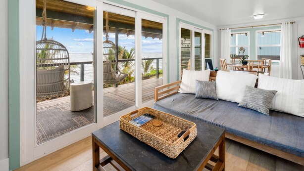Uma sala ampla com uma grande janela com vista para uma varanda, um espaço de estar confortável e uma mesa de madeira com uma cesta de vime.
