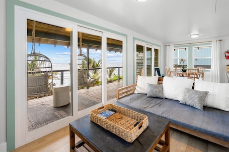 A spacious living area with a large window overlooking a balcony, a comfortable seating area, and a wooden table with a woven basket.