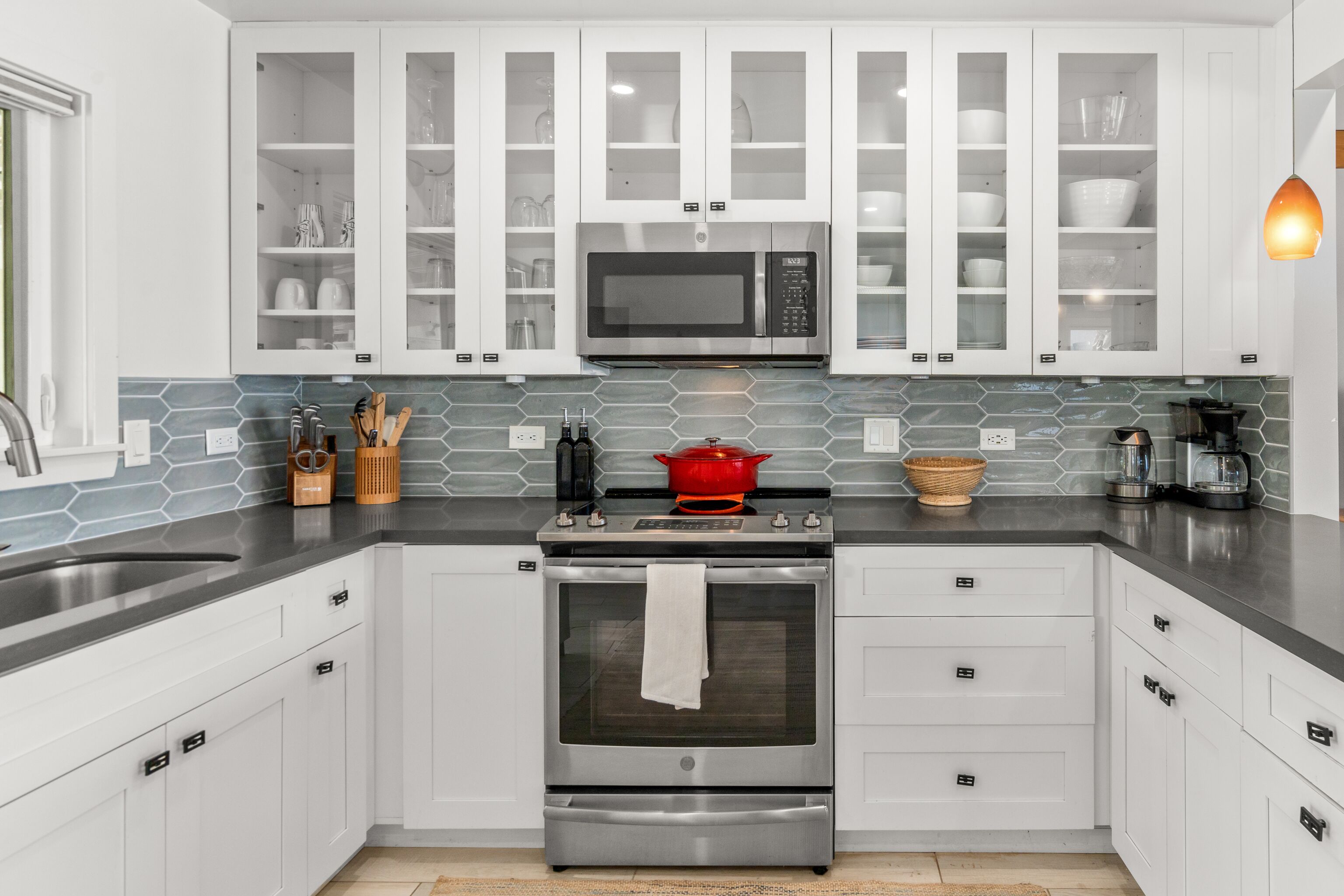 Una cocina moderna con gabinetes blancos, un horno de acero inoxidable, un microondas y una olla roja en la estufa.