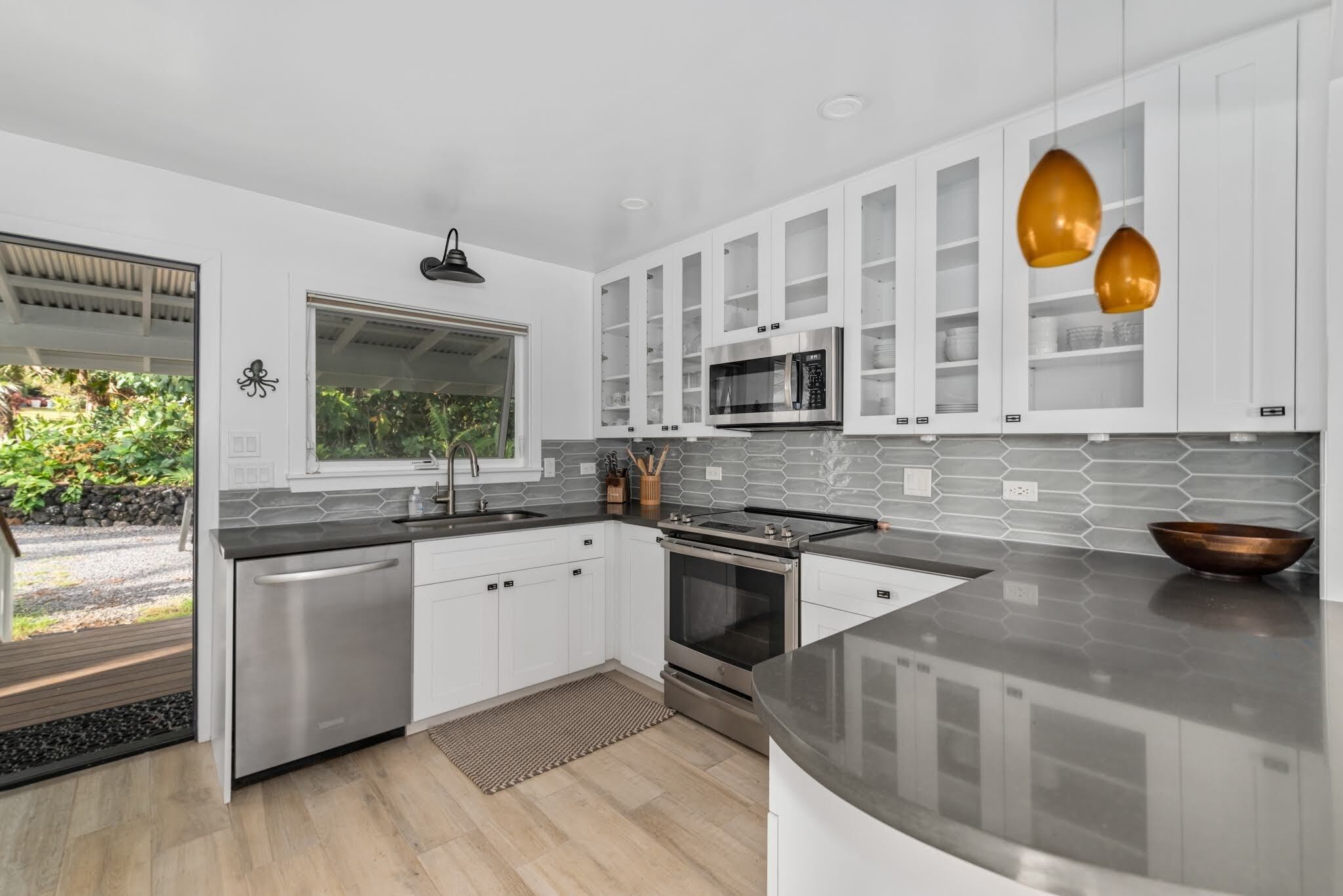 A modern kitchen with white cabinets, stainless steel appliances, and a large window.