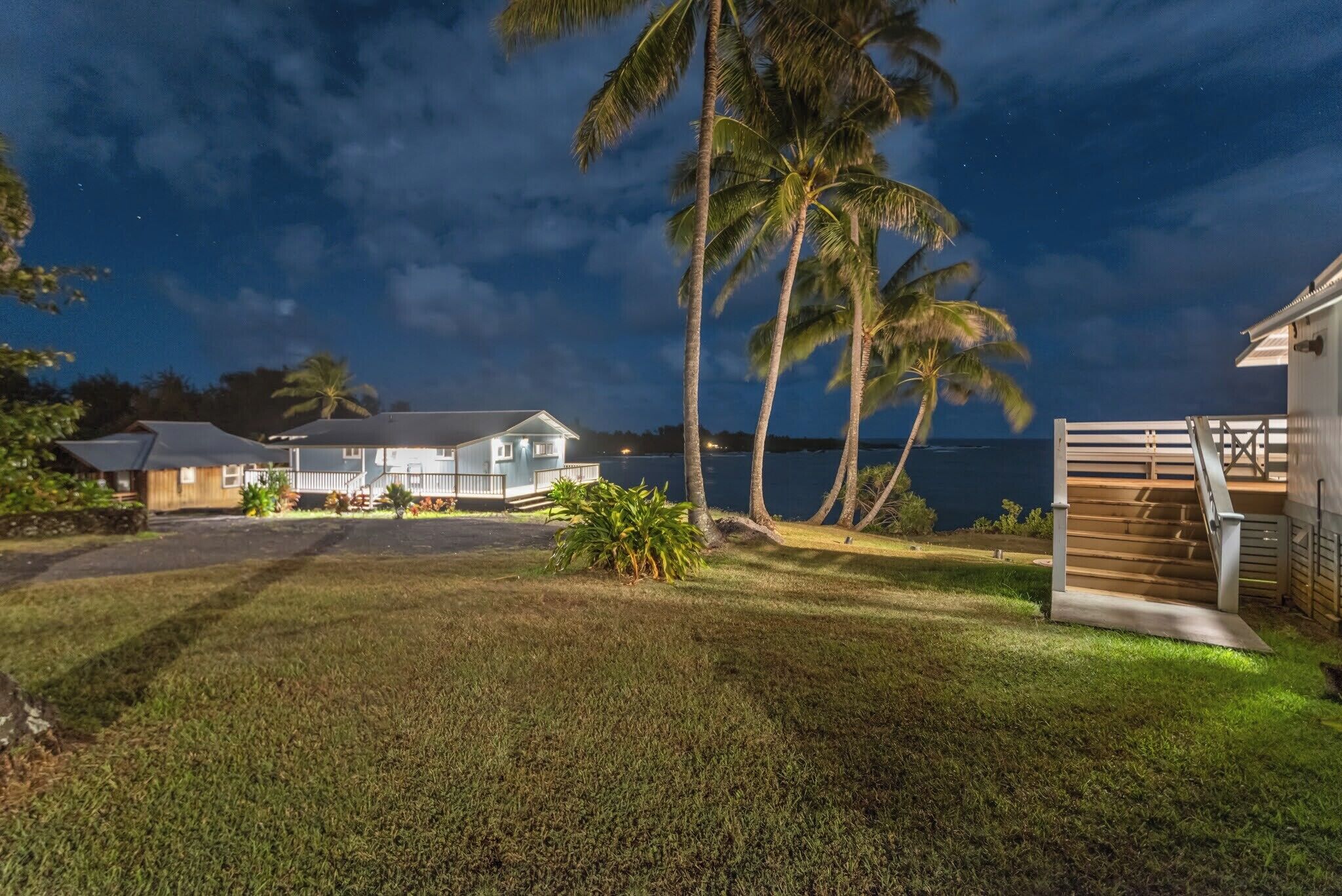 A house with a well-maintained lawn, a wooden staircase, and a view of the ocean at night.