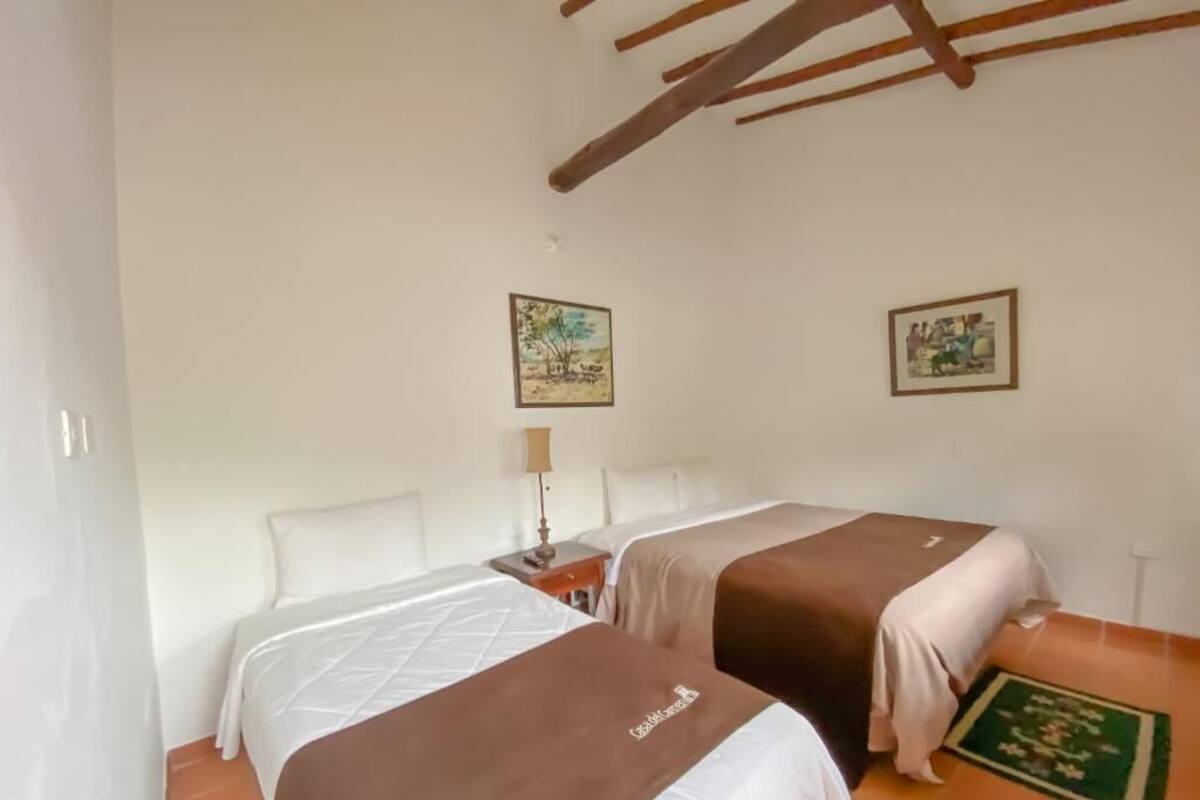 Ein Zimmer mit zwei Betten, einem Nachttisch, einer Lampe und zwei gerahmten Bildern an der Wand.