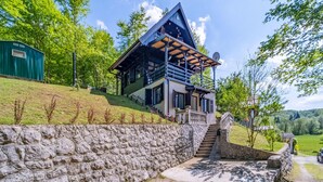 A modern house with a stone retaining wall, a wooden staircase, and a green building in the background.