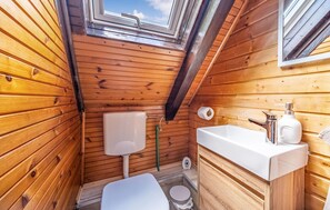 Een klein houten badkamertje met dakraam, toilet, wastafel en douche.