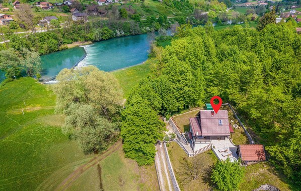 Luchtbeeld van een pand met een rivier, weelderige begroeiing en een rode markering voor de locatie.