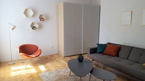 A modern living room with a grey sofa, orange chair, and a coffee table. There are hexagonal shelves on the wall and a large wardrobe. - Explore Bellingham, minutes Airport WWU & Downtown (Bellingham)