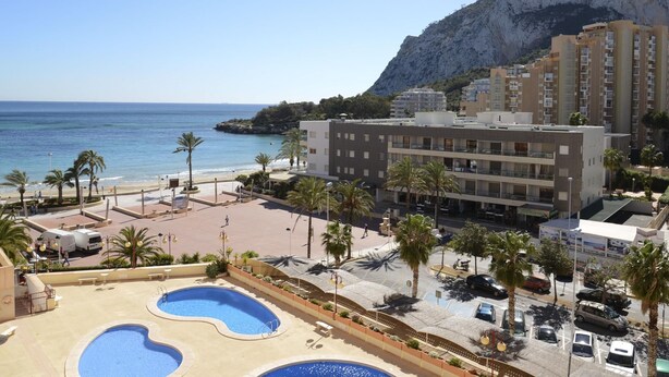 A resort with a pool area, a beach, and a mountain backdrop.