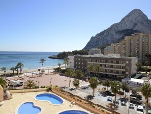 A resort with a pool area, a beach, and a mountain backdrop.