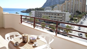 A balcony with a table set for two, overlooking a coastal town with buildings and a mountain in the background.