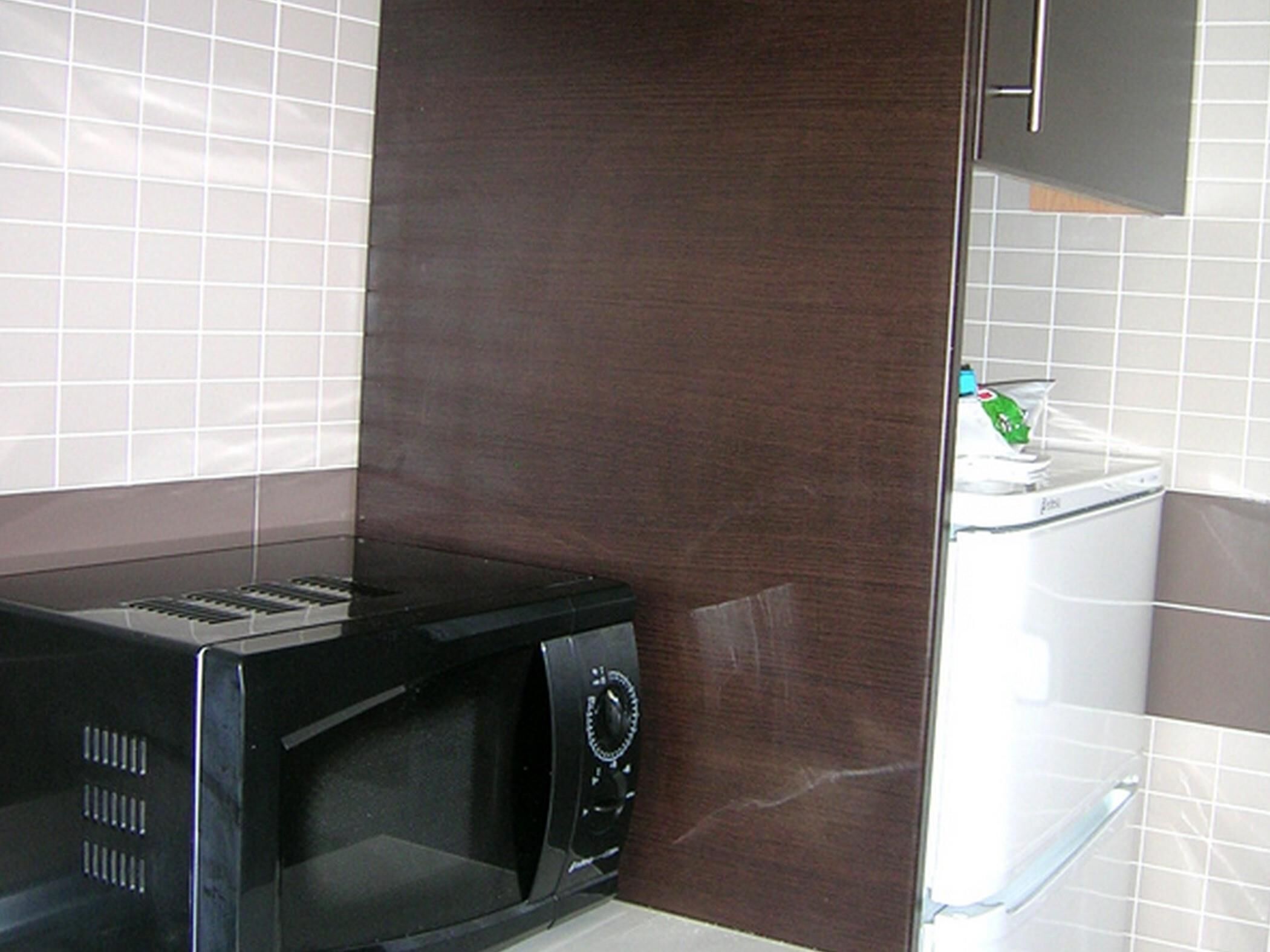 A kitchen with a black microwave, a white washing machine, and a wooden cabinet.