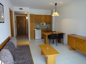 Un espacio habitable compacto con kitchenette, un sofá, una mesa de comedor y una pequeña zona de cocina.