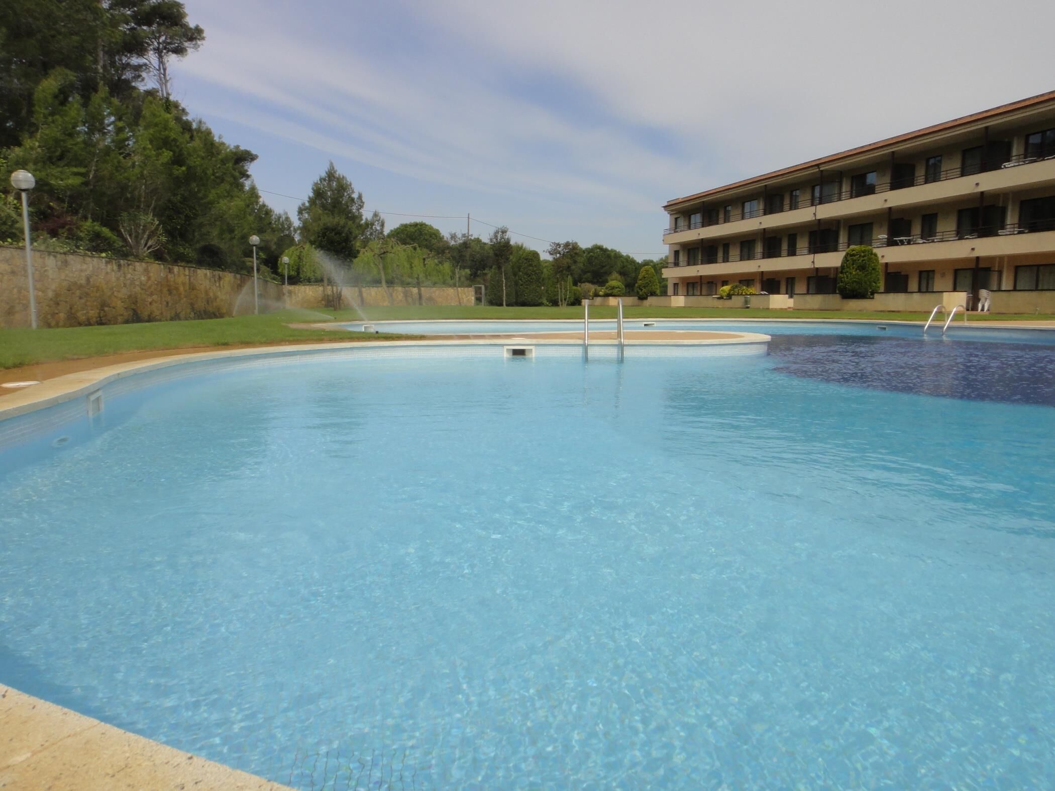 Ein Swimmingpool mit klarer, blauer Wasseroberfläche, umgeben von einer Steinmauer und einem Gebäude mit mehreren Balkonen.