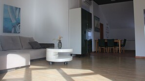 Una sala moderna con un sofá, una mesita auxiliar blanca y una zona de comedor con sillas y una mesa.