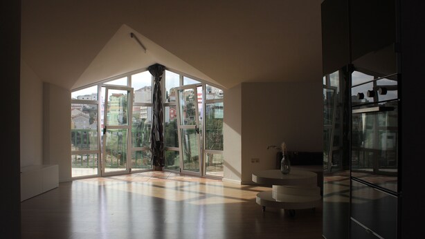 Una habitación amplia con ventanas grandes, un sofá blanco moderno y un aparador de vidrio.