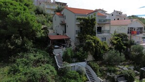 Un edificio residencial con varios balcones, una escalera que lleva a los pisos superiores y abundante vegetación circundante.