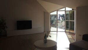 Una sala de estar moderna con un televisor de pantalla plana, una mesa de centro redonda con un florero y un ventanal corredero que da a un balcón.
