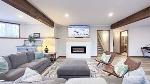 A modern living room with a fireplace, a sofa, a coffee table, and a TV mounted above the fireplace. - Lakeside Layover, King Bed, Sauna! (Bayfield)