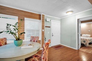 A dining area with a round table, chairs, a potted plant, and a door leading to a bedroom. - Historic District Bungalow: BBQ, Bikes & Beach Kit (St. Augustine)