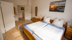 Un dormitorio con cama, cabecera de madera, mesitas de noche, lámpara, espejo y un cuadro de un atardecer.