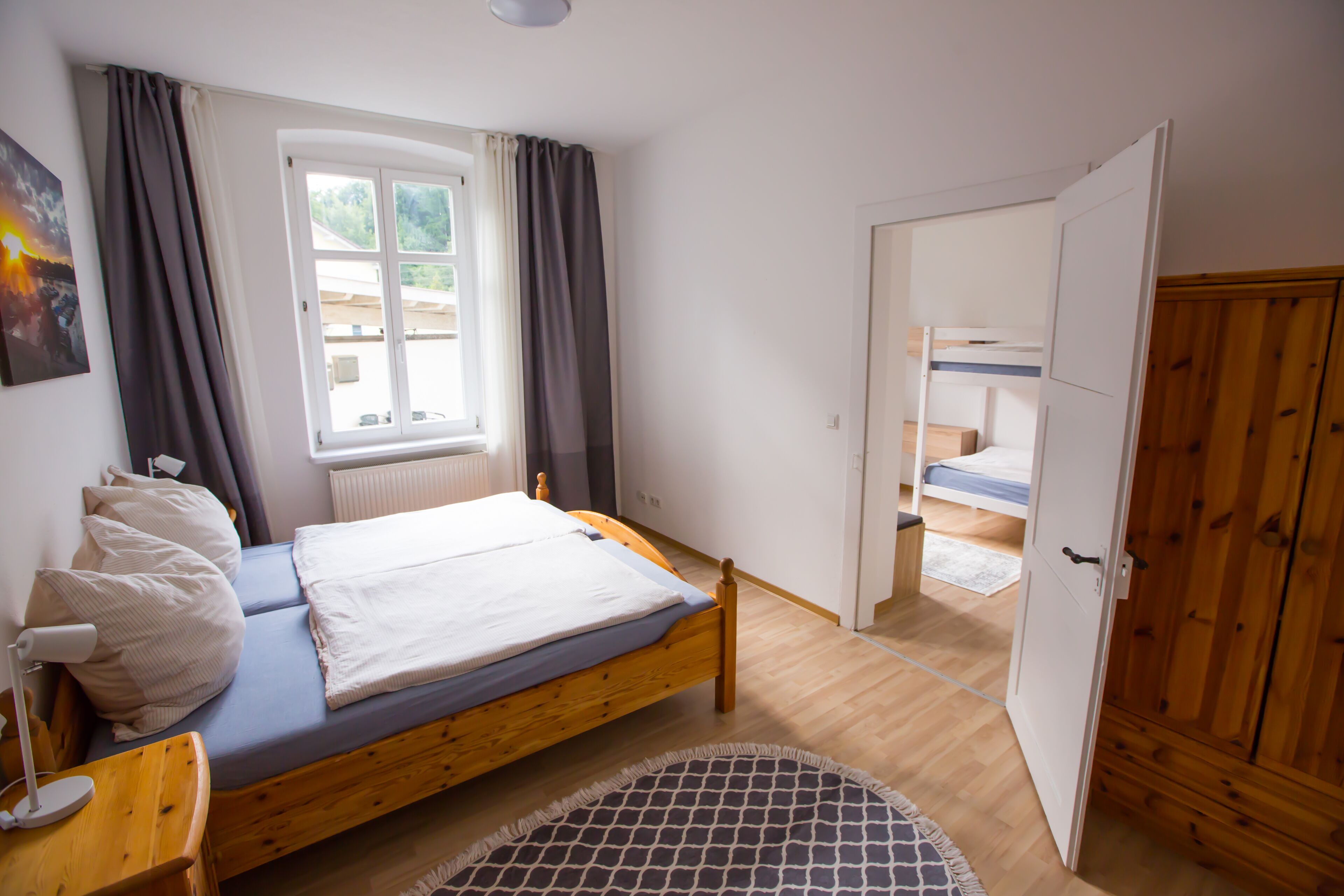 A bedroom with a single bed, a wooden wardrobe, and a window with curtains.