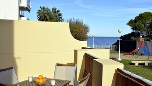 A patio with a table, chairs, and a bowl of fruit. There is a view of the sea and a playground in the background. - Anacasa Caleta Denia Marines PB2213 (Denia)