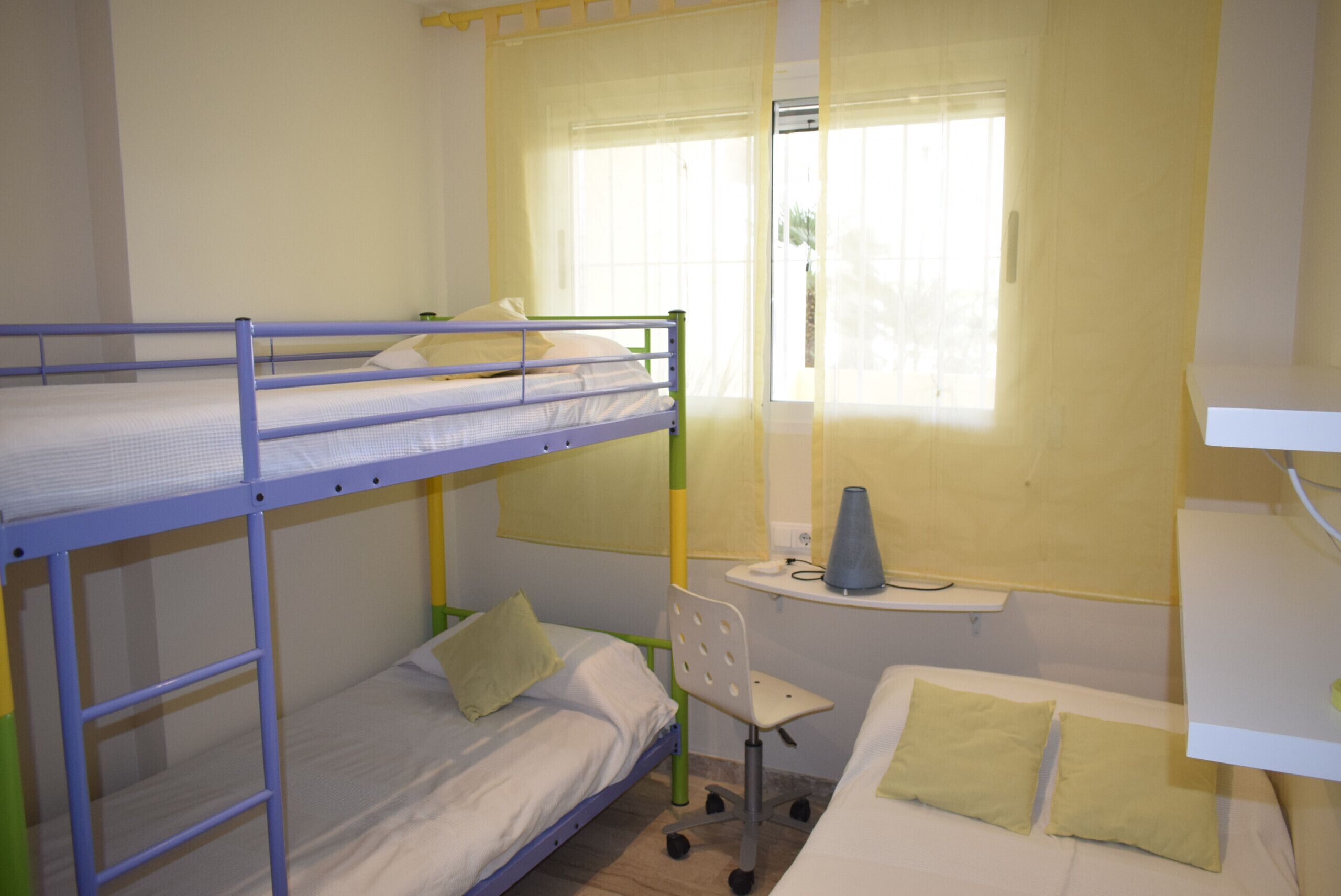 A dormitory room with bunk beds, a desk, and a chair.