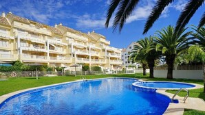 A swimming pool with a curved design, surrounded by a well-maintained lawn and palm trees. - Anacasa Caleta Denia Marines PB2213 (Denia)