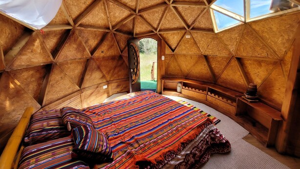 A cozy, triangular room with a bed, a wooden bench, and a small table.