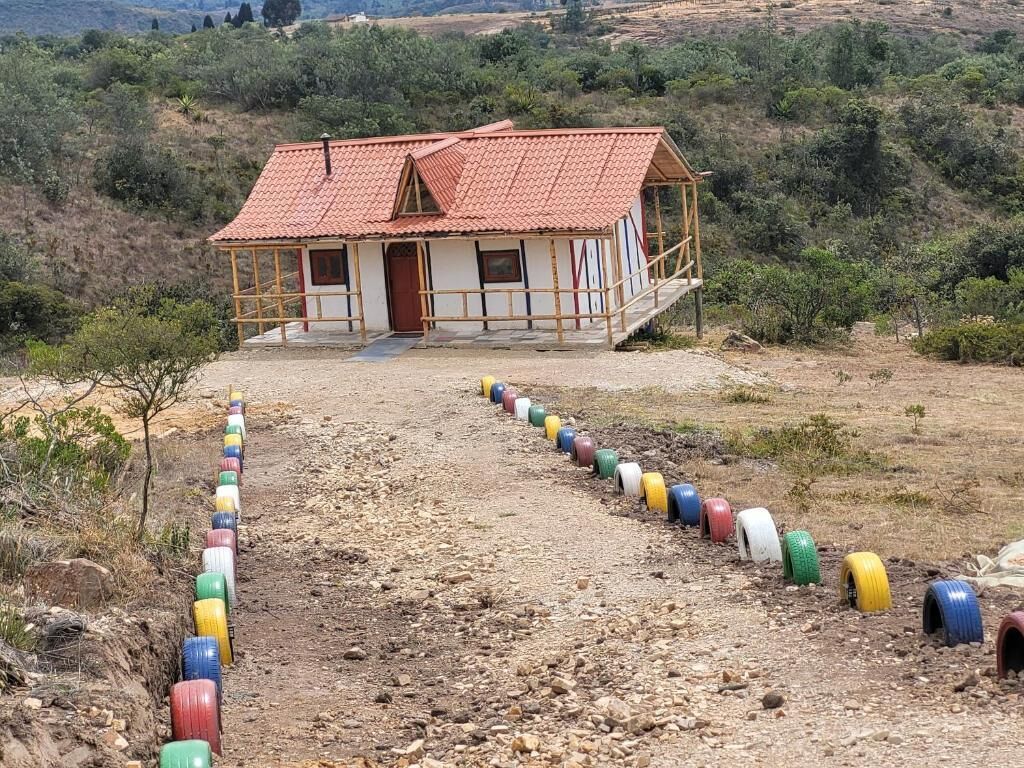 A small house with a red-tiled roof and a porch, surrounded by a gravel path lined with colorful tires.
