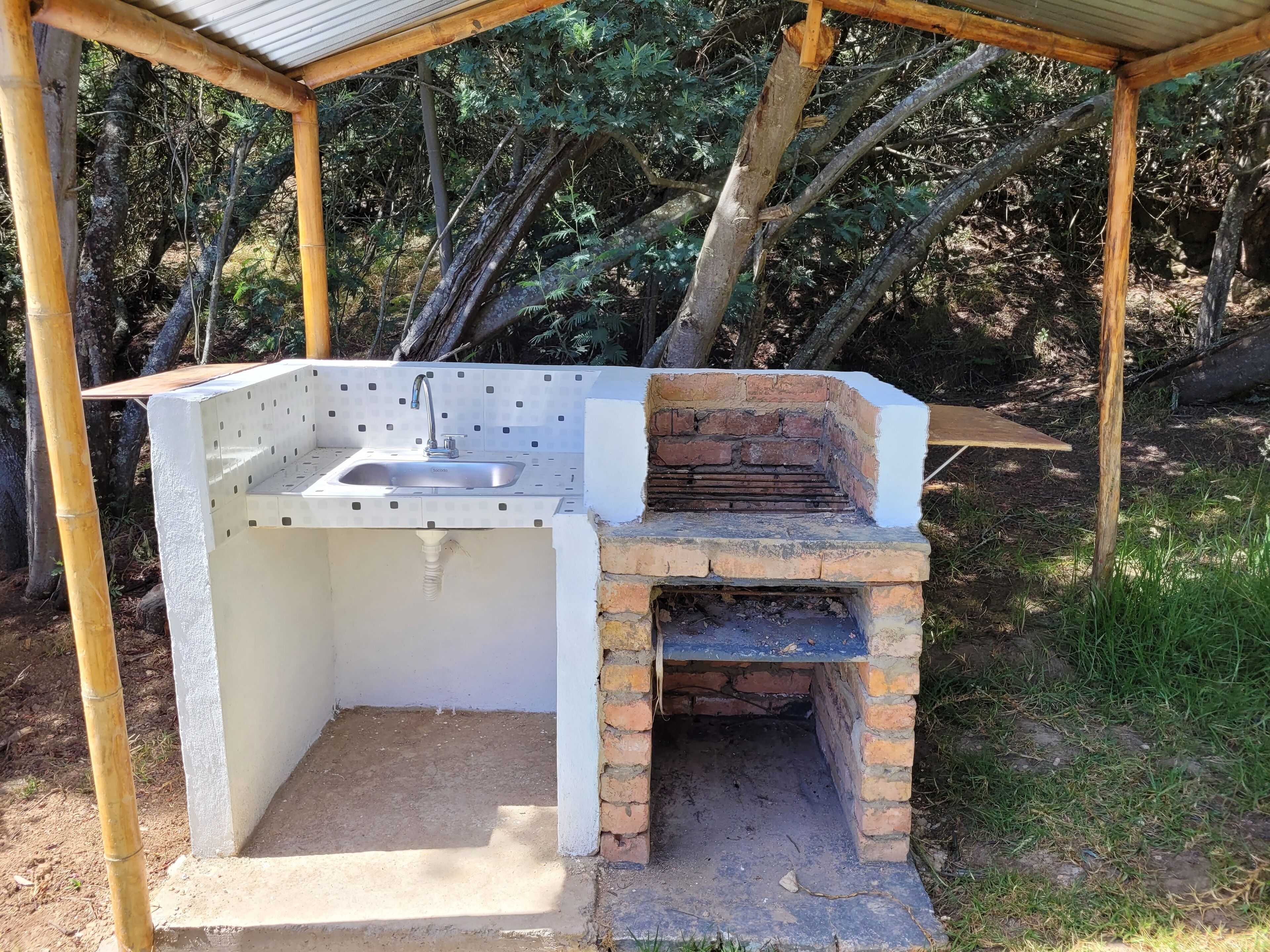 An outdoor kitchen with a sink and a brick oven, surrounded by trees.