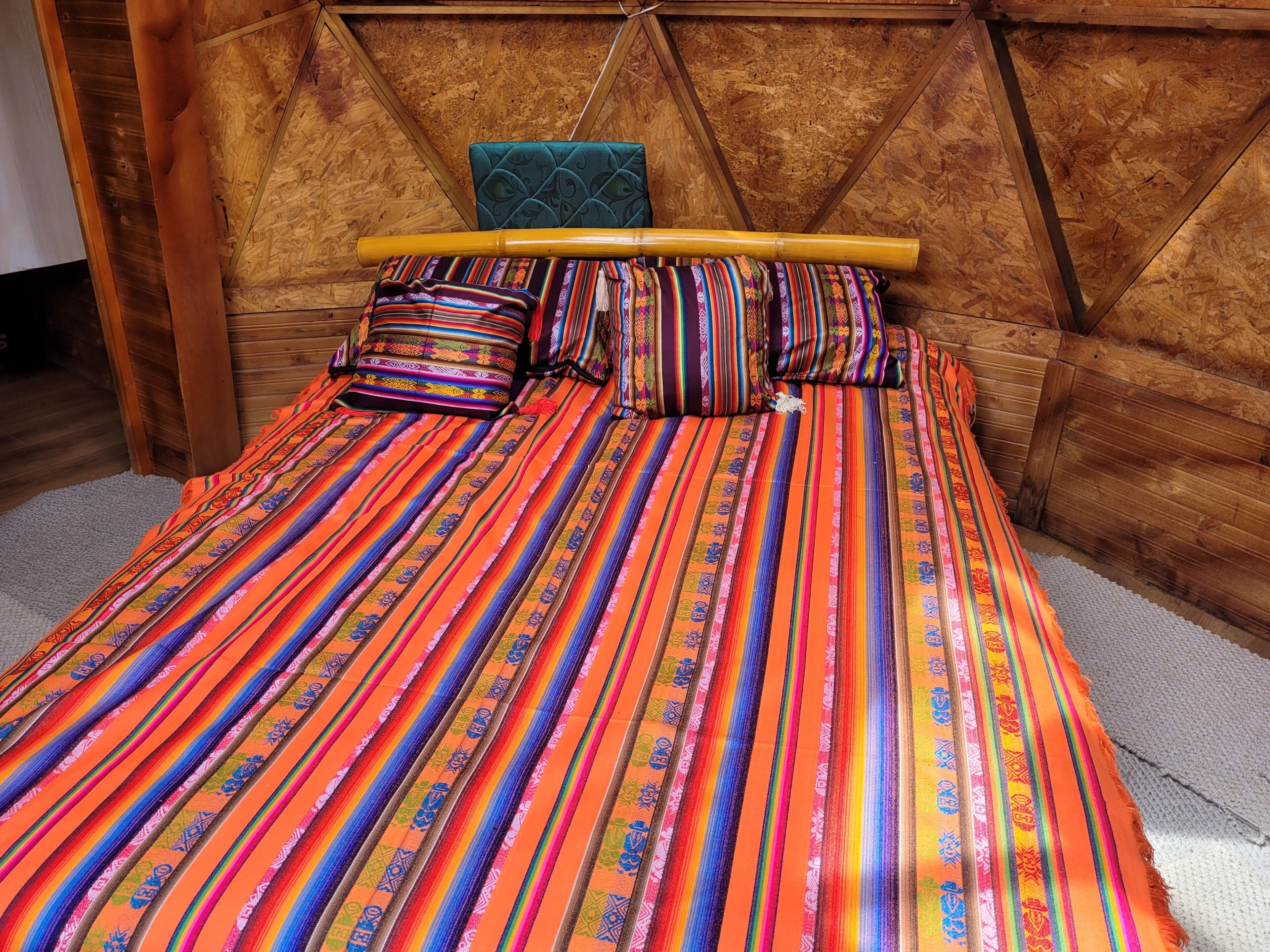 Una cama con una colcha a rayas de colores y almohadas, cabecera de madera y suelo de madera.