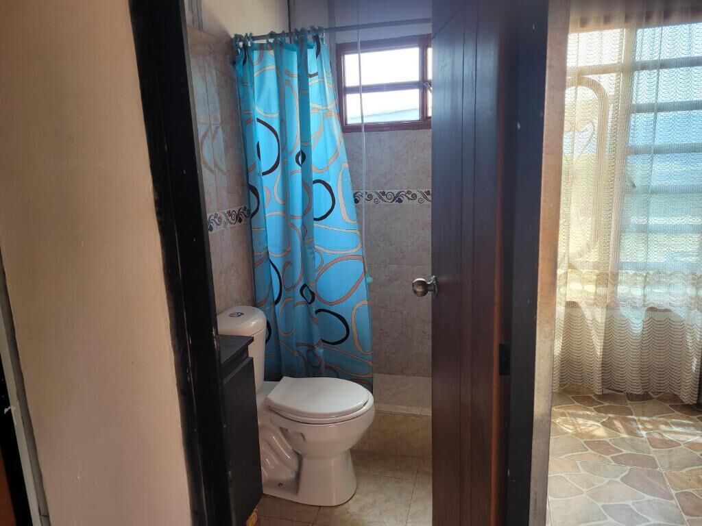 Un baño con inodoro, cortina de ducha y ventana.