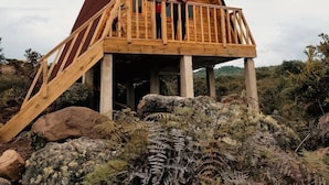A wooden cabin with a balcony, situated on rocky terrain with ferns.