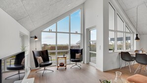 Ein geräumiges Wohnzimmer mit großen Fenstern, modernen Möbeln und Blick ins Freie.