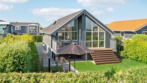 Ein modernes Haus mit großer Glasfront, überdachter Veranda und gepflegtem Garten.