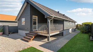 Ein modernes Einfamilienhaus mit Satteldach, einer Veranda mit Geländer und einer kleinen Treppe zum Eingang.