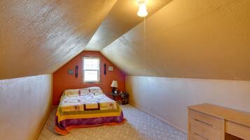 A bedroom with a sloped ceiling, a bed with a colorful quilt, a small table with a lamp, and a dresser.