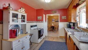 A compact kitchen with a stove, sink, and cabinets. There is a dining area with a table and chairs visible through an open door. - Charming 'Corral Creek Ranch House' in Circle (Circle)