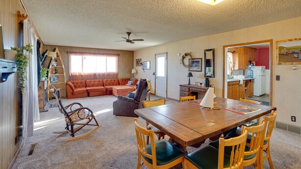 A spacious living area with a wooden dining table, a rocking chair, and a sofa. There is a kitchen visible through an open doorway. - Charming 'Corral Creek Ranch House' in Circle (Circle)