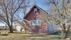 A red wooden house with a garage, surrounded by trees and a gravel driveway. - Charming 'Corral Creek Ranch House' in Circle (Circle)