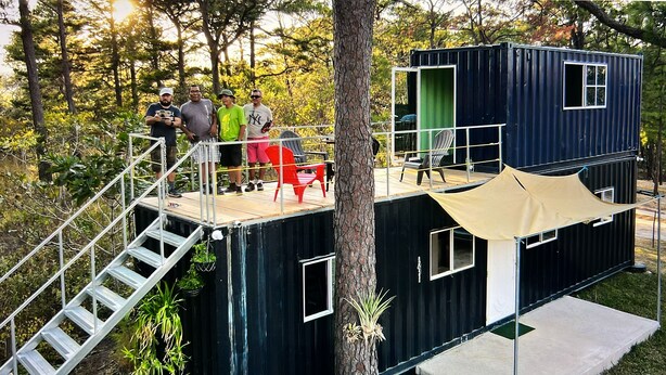 A multi-level modular cabin with a staircase, outdoor seating, and a green door.