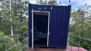 A wooden deck leading to a blue container with a bed inside.