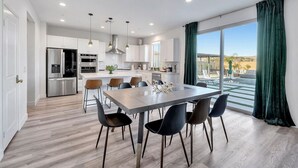 Una cocina moderna con electrodomésticos de acero inoxidable, un comedor con una mesa grande y sillas, y vistas al exterior a través de amplias ventanas.