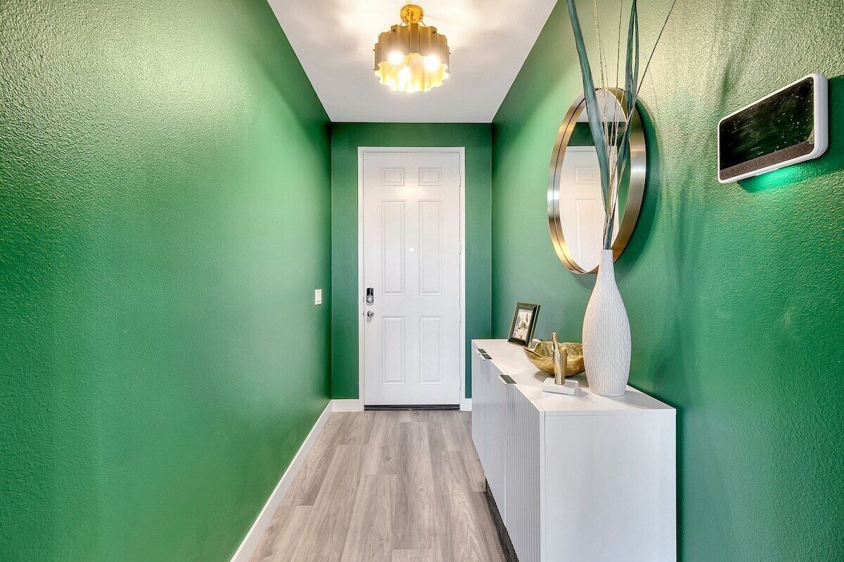 A hallway with green walls, a white door, and a white reception desk with a vase and picture frame.