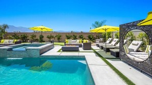 Zona junto a la piscina con sillas de descanso y sombrillas, un brasero y vistas a las montañas.