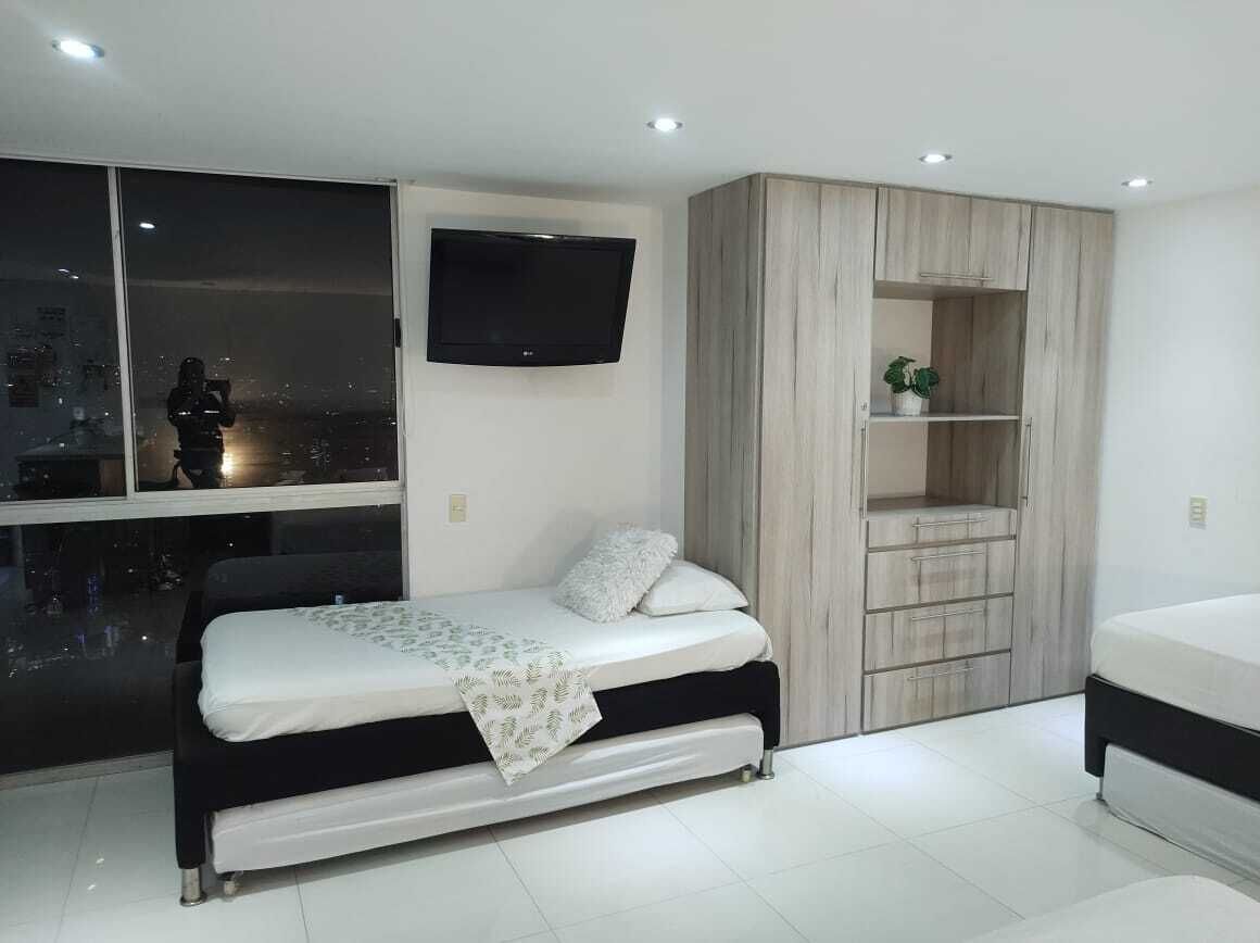 Une chambre à coucher moderne avec un lit, un téléviseur fixé au mur, une grande fenêtre et une armoire intégrée.
