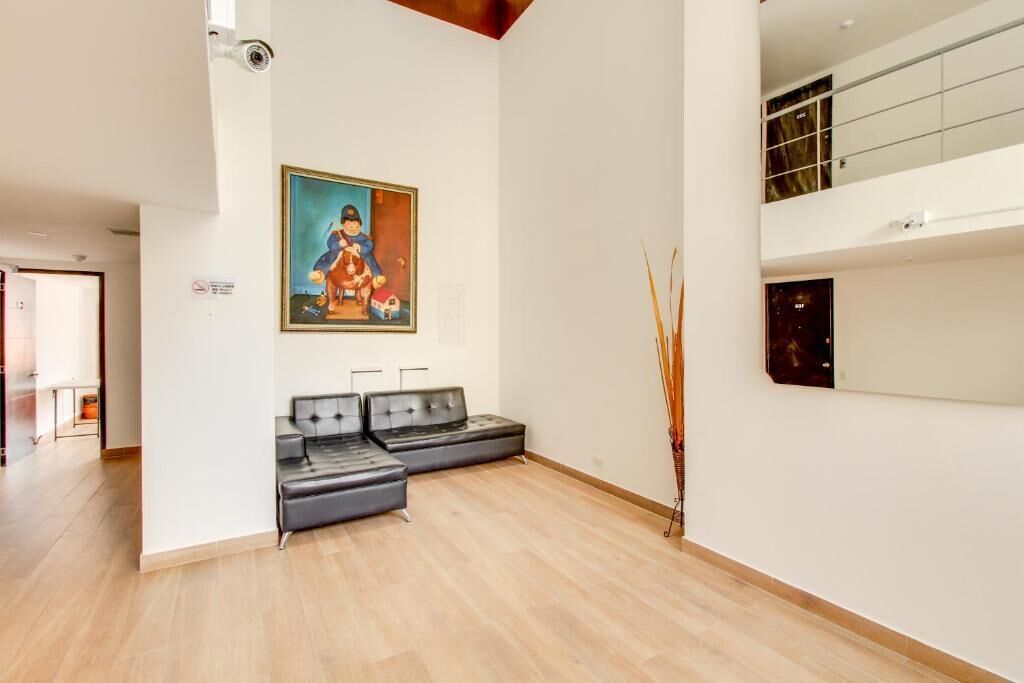 Um quarto espaçoso com um sofá de couro preto, uma pintura na parede e uma planta alta.