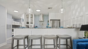 Een moderne keuken met witte kasten, een roestvrijstalen koelkast en een bar met krukken.
